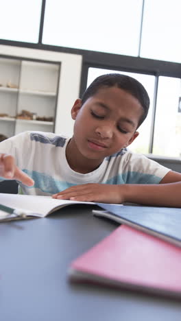vertical video: in school, boy reading book and focusing on studying in classroom