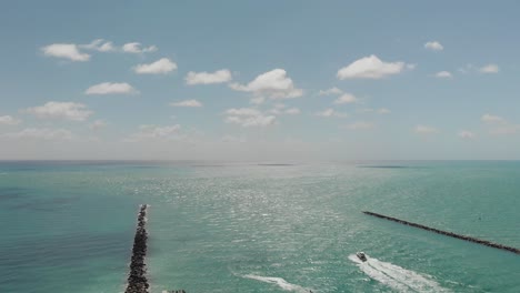 aerial view of the ocean in miami beach, a boat sails towards the ocean between breakwaters, slow motion