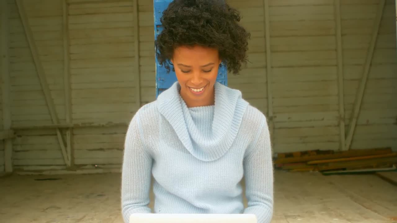 젊은 아프리카계 미국인 여성이 해변 오두막 4k에서 노트북을 사용하고 앉아 있습니다.