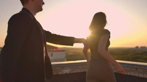 Young-couple-holding-hands-walking-woman-leading-boyfriend-the-roof-of-the-building-at-sunset-POV-travel-concept.-Carefree-free-lovers-run-on-the-roof-laughing-and-smiling