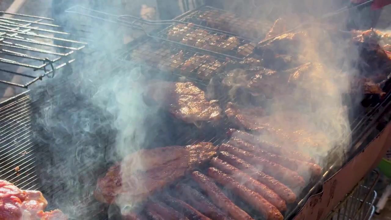 Primo piano di varie carni e salsicce che grigliano su un barbecue a carbone con fumo denso.