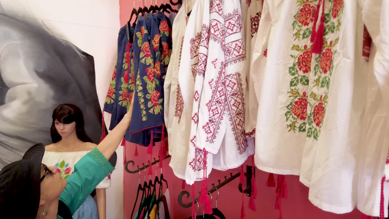 Mature woman looks at beautiful display of women’s huipil blouses in Merida Mexico store