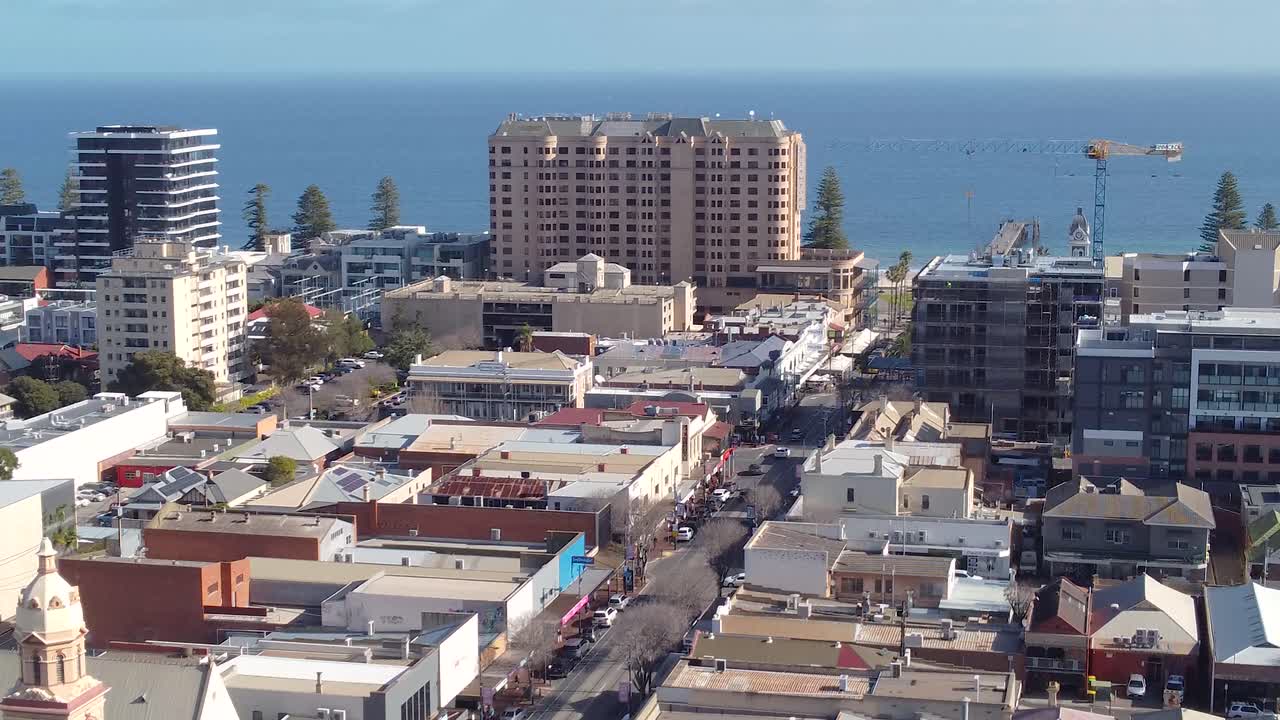 A drone shot looking down on the Glenelg beachside precinct near Adelaide in South Australia. The shot shows Jetty Road, hotels, the Glenelg beach foreshore, and the ocean. Great tourism content.