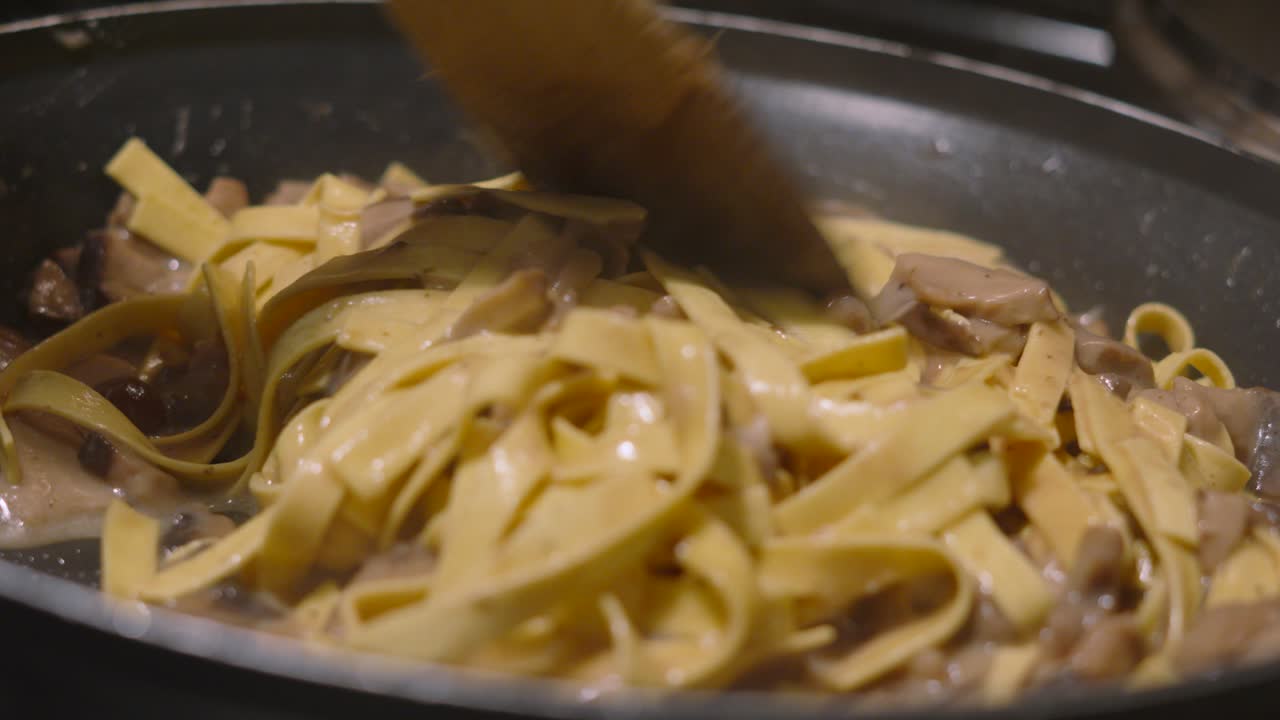 Wooden Spatula Moving Italian Mushroom Tagliatelle Around Hot Pan with Various Fungi Including Champignon, Shitake, Nameko. Home Cooked Cream Sauce Based Pasta Dish.