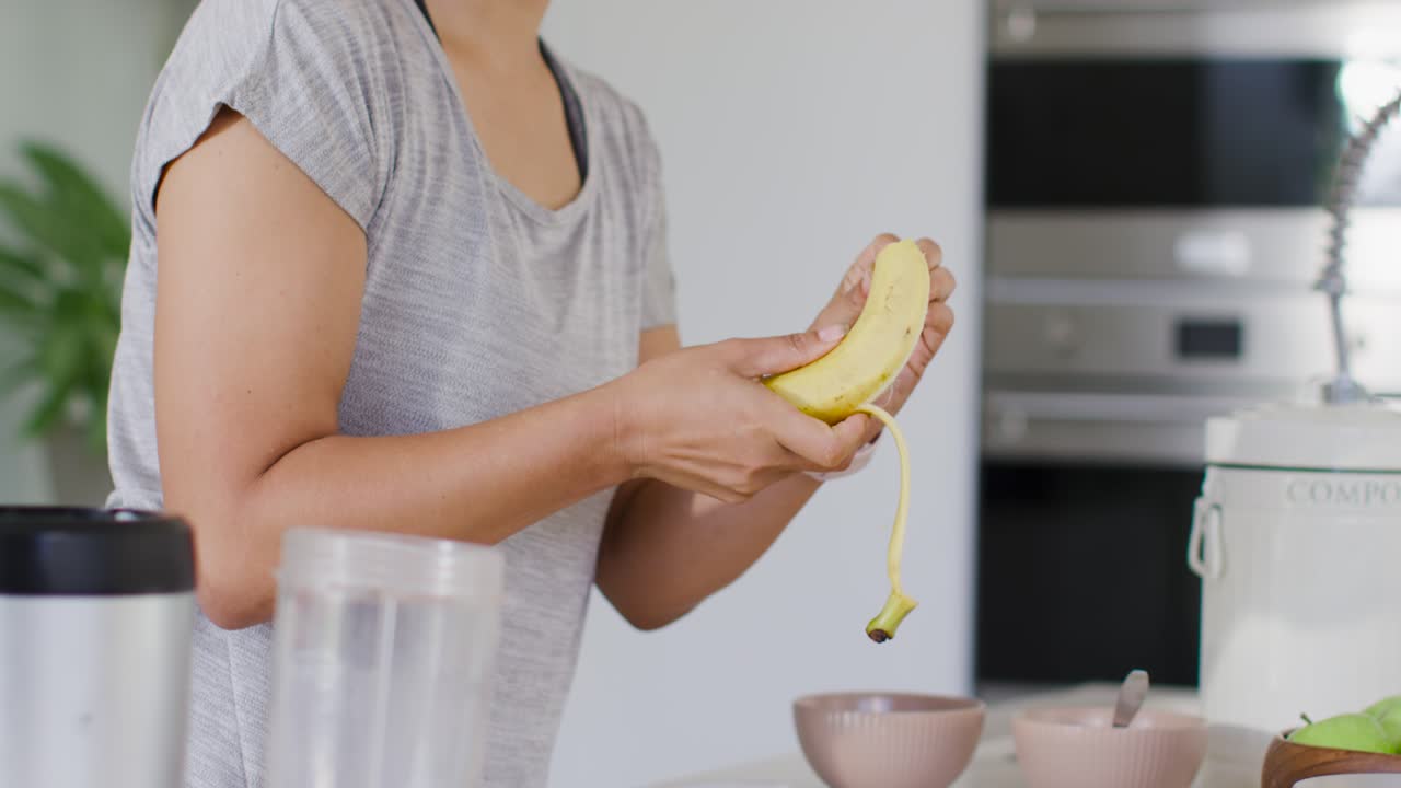 Mujer inspeccionando un plátano en la encimera de la cocina, pelándolo en secciones para el vaso de la batidora.