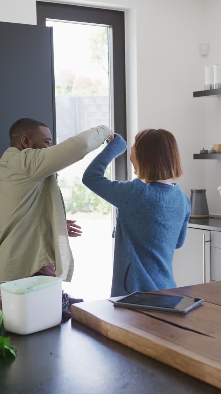 video vertical de una pareja feliz y diversa divirtiéndose bailando juntos en la cocina