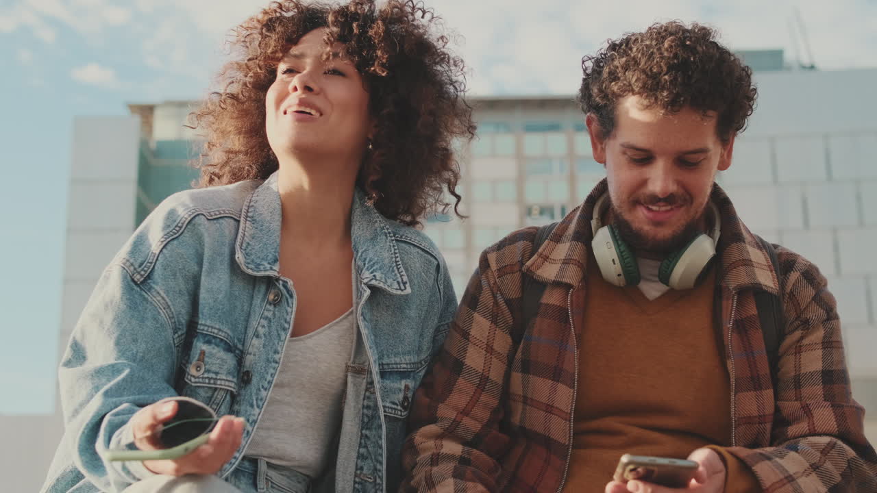 Couple with curly hair using smartphones outdoors