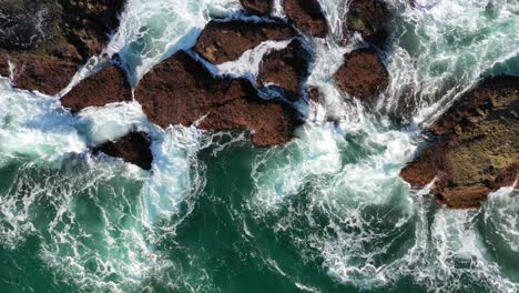 foamy waves splashing on huge rocks of the beach - aerial top down