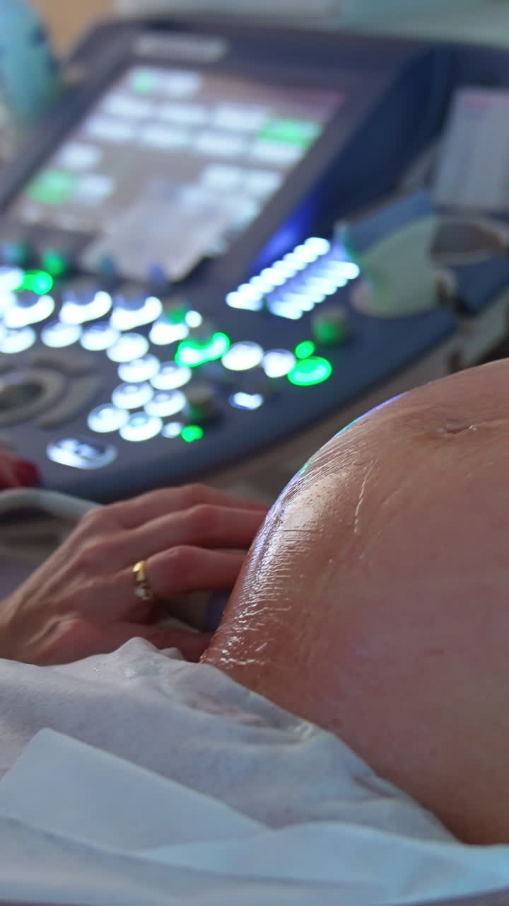 Big abdomen covered with gel of a pregnant lady. Doctor does the ultrasound examination to a future mom at last months of pregnancy. Vertical video