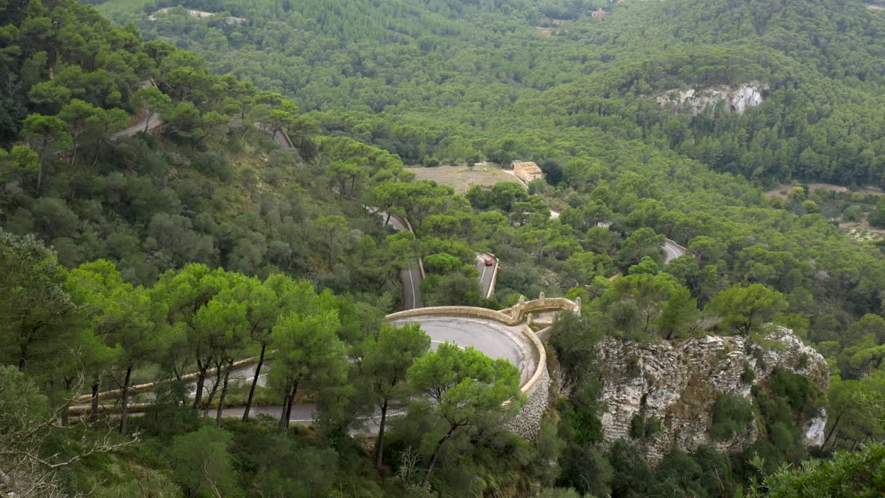 Auto che guidano su una strada tortuosa in montagna, parzialmente coperta da alberi