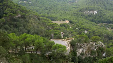 cars driving on a curvy road i the mountains, partly covered by trees