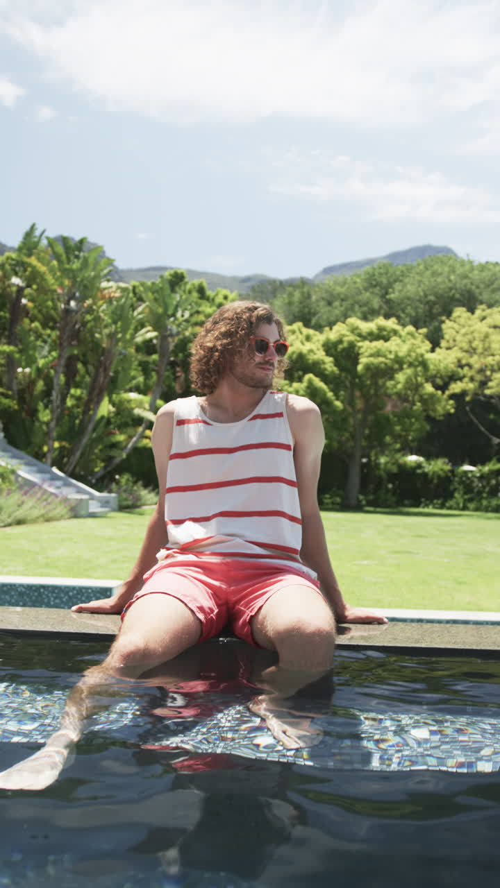 Vertical video: Caucasian male relaxing by pool, greenery around, at home