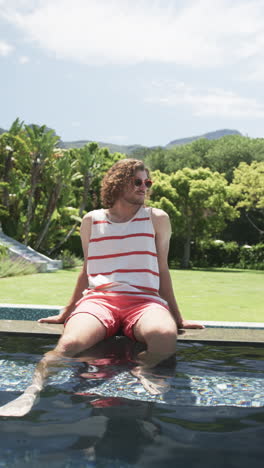 vertical video: caucasian male relaxing by pool, greenery around, at home