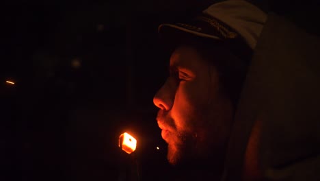 guy blowing coal with ember in dark background. close up, side view