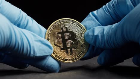 hands wearing gloves holding bitcoin crypto currency coin against dark background, close up