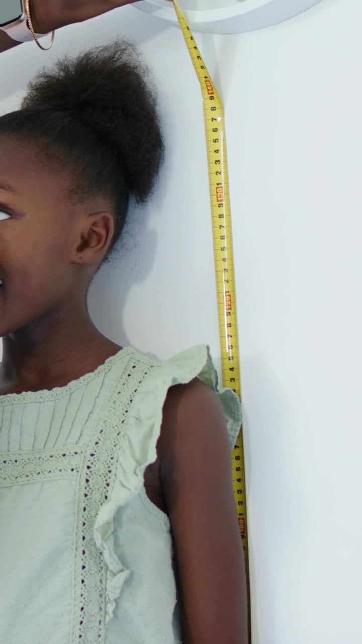 Vertical video: Placing adult moving yellow tape by child in dress at home, taking height, watch