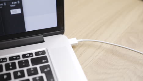 close view of white usb cable being plugged in and out of laptop