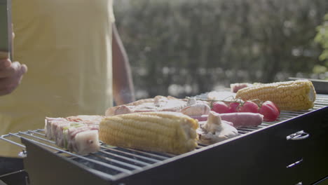 man with tweezers watching grilling meat and vegetables