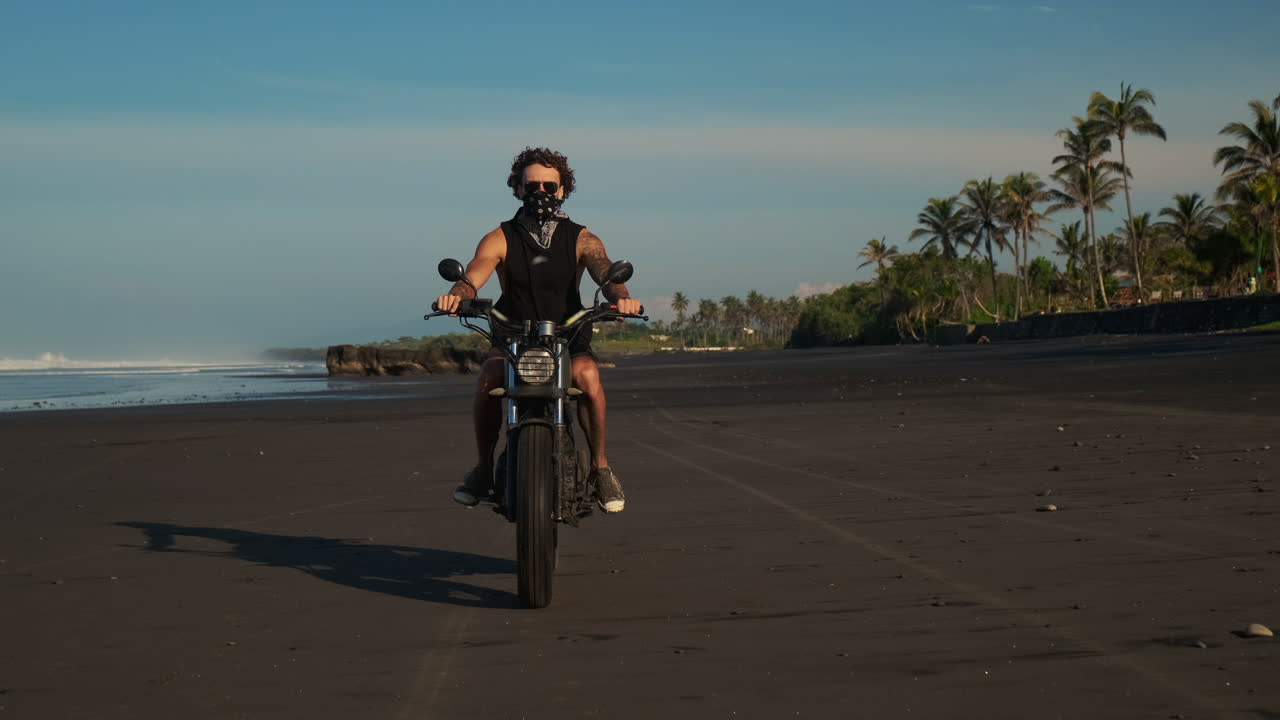 человек едет на мотоцикле по черному песчаному пляжу