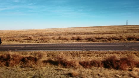 Black-all-terrain-car-driving-on-a-highway-in-a-dry-and-desert-landscape-and-cloudless-blue-sky