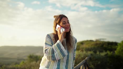 attractive young woman making a cell phone call while smiling with sunset behind her