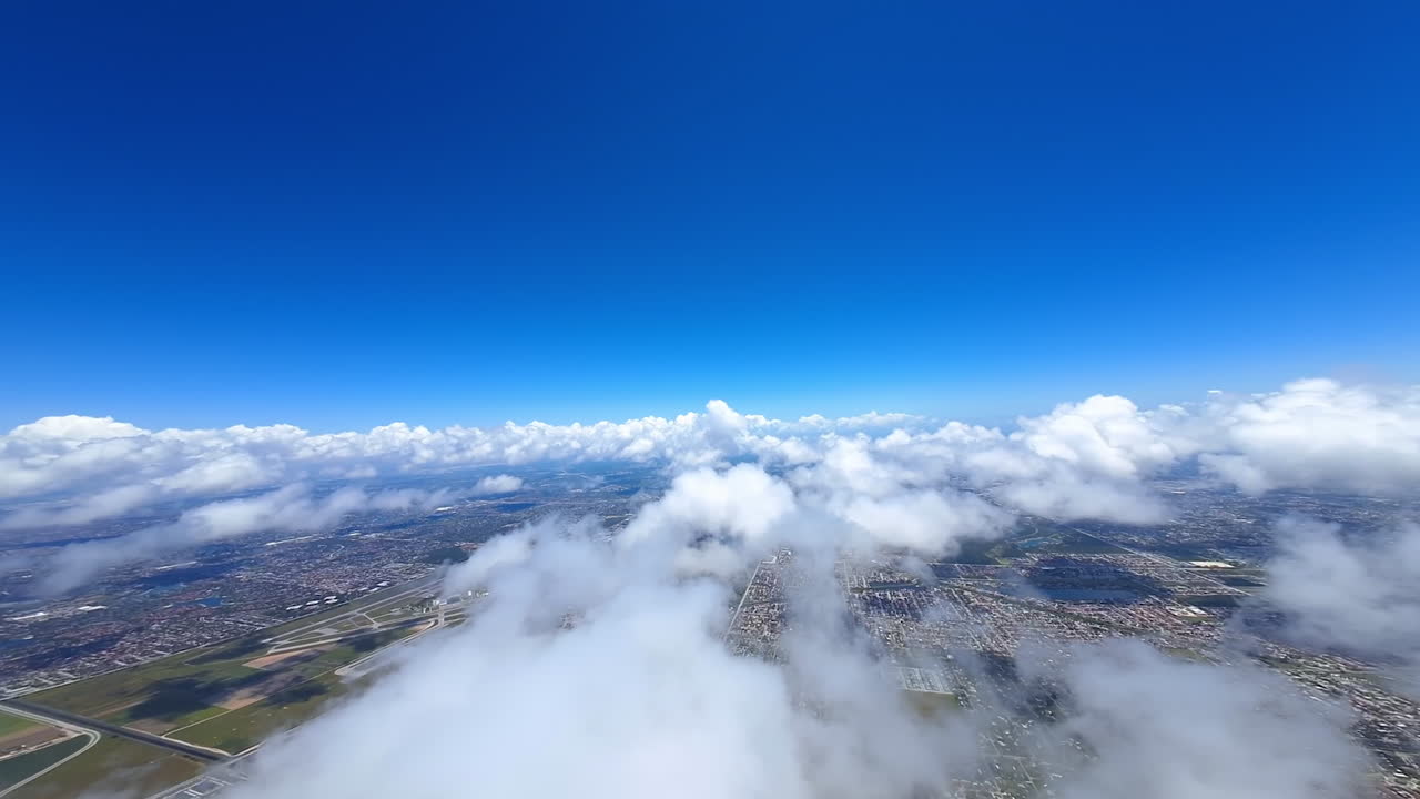 Stunning white cloudscape in the azure sky. FPV drone moving above the clouds opening view on the urban landscape on the ground.
