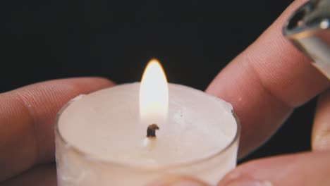 man-lights-candle-in-plastic-holder-on-dark-background