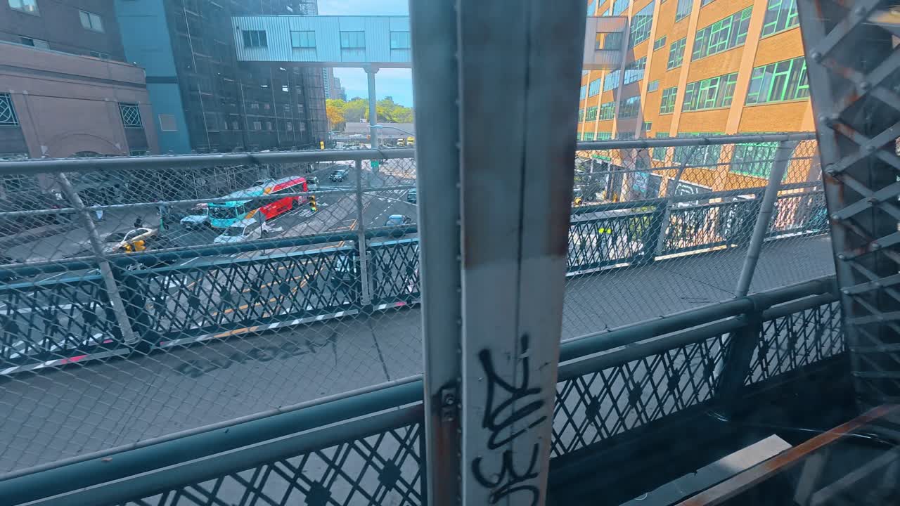 New York, USA, 1 aprile 2026: Struttura in acciaio industriale di un ponte con edificio cittadino sullo sfondo. Primo piano di tralicci di ponte usurati con graffiti che si affacciano su un edificio industriale urbano con finestre verdi.