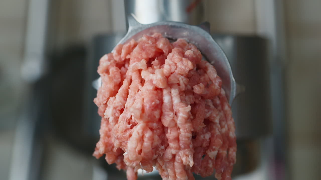 Carne moída sai de um moedor de carne.