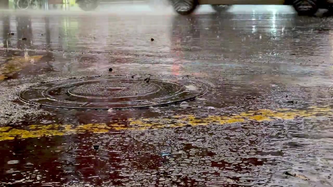 Flooded street with manhole cover during heavy rain at night