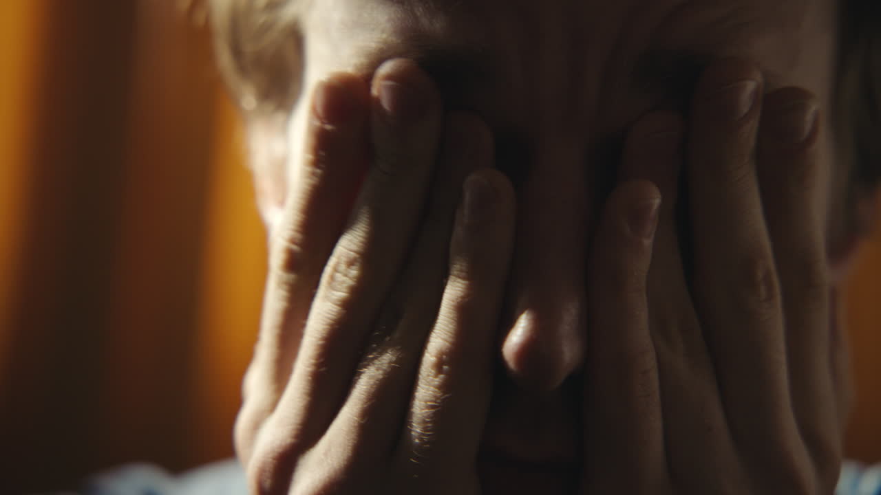 Close-up of a man with his eyes closed and hands covering his face