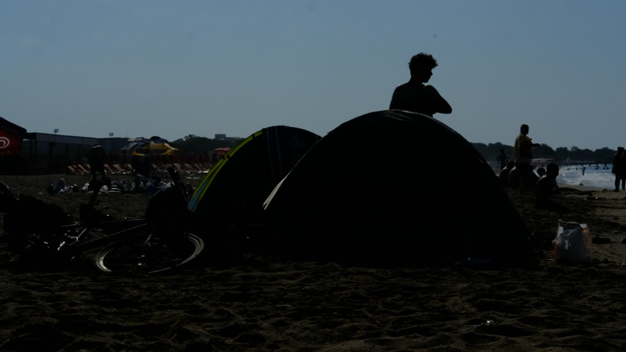 실루 ⁇  젊은 남자가 텐트를 집어 들고 있습니다.