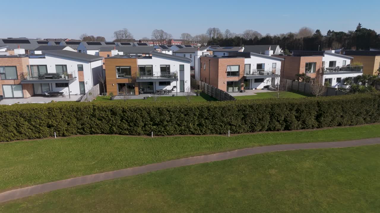 Aerial push-in over luxury modern housing estate with solar-clad roofs, bold clean lines, manicured lawns and spacious plots conveying sustainable upscale residential living