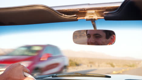 young white man driving an open top car, face seen in mirror