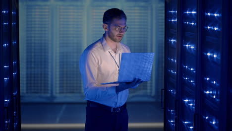 male server engineer in data center. it engineer inspecting a secure server cabinet using modern technology laptop coworking in data center.