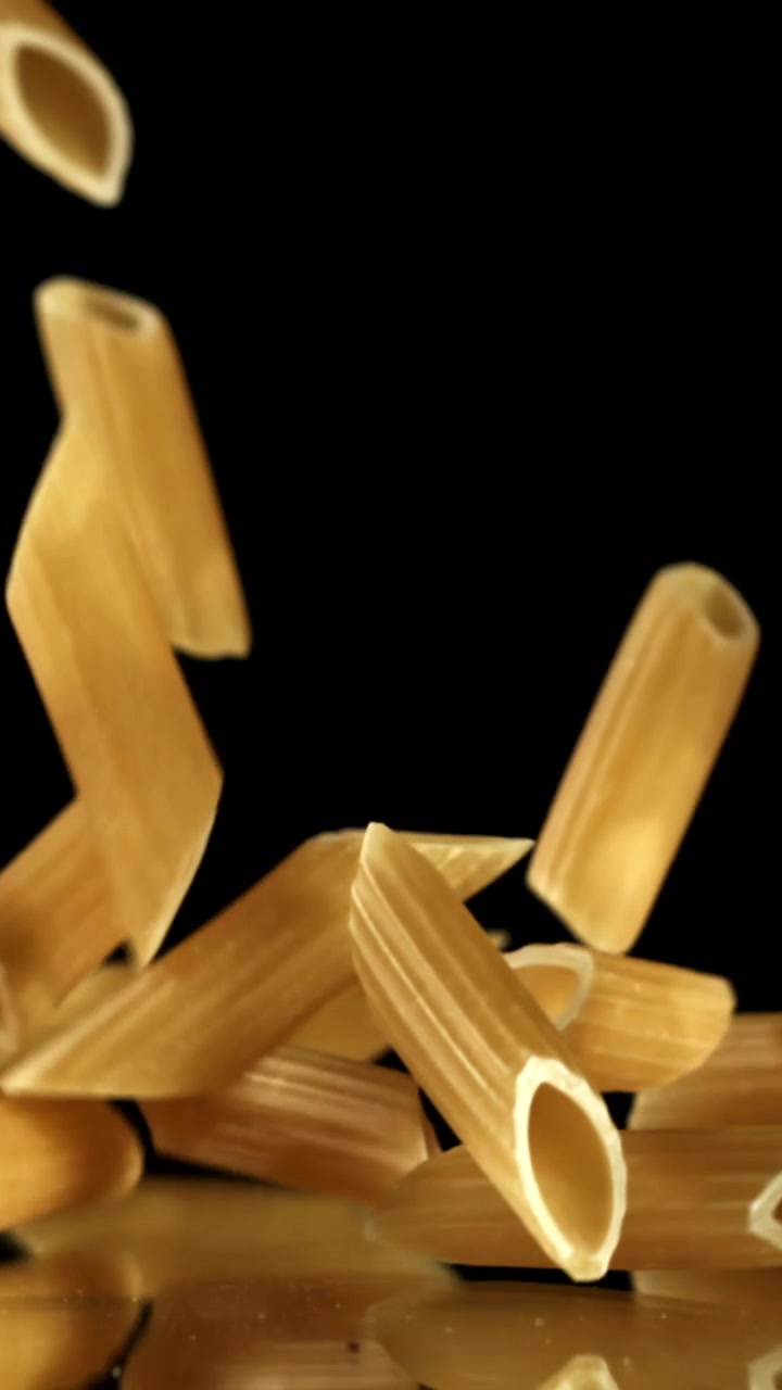 Pasta penne cruda che cade al rallentatore su sfondo nero
