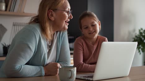 Caucasian-grandmother-and-granddaughter-having-video-call-via-laptop-in-the-kitchen