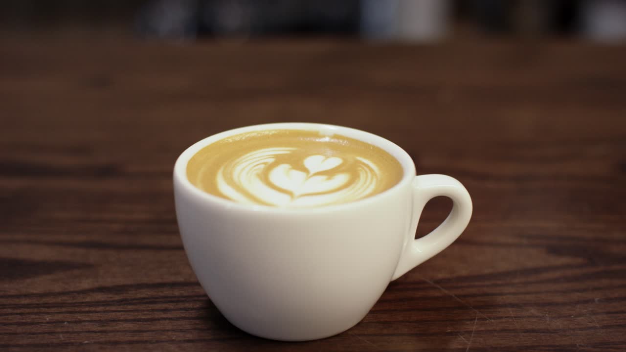 한 손 이 나무 테이블 을 가로질러 라테 를 미끄러뜨린다