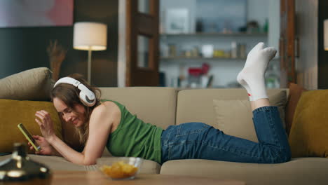 Mujer-Sonriente-Escuchando-Auriculares-Tumbados-En-El-Sofá.-Niña-Feliz-Y-Relajada-Moviendo-La-Cabeza