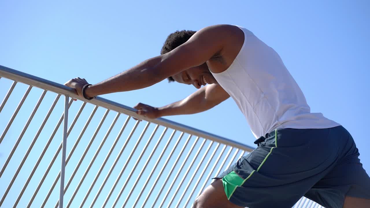 un atleta afroamericano sonriente haciendo ejercicio contra el cielo azul