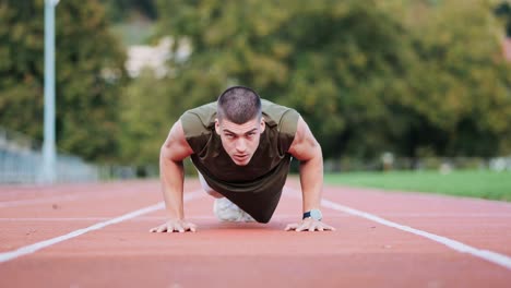 Athletic-young-man-training-with-push-ups-on-the-rattling-track-of-a-sports-facility