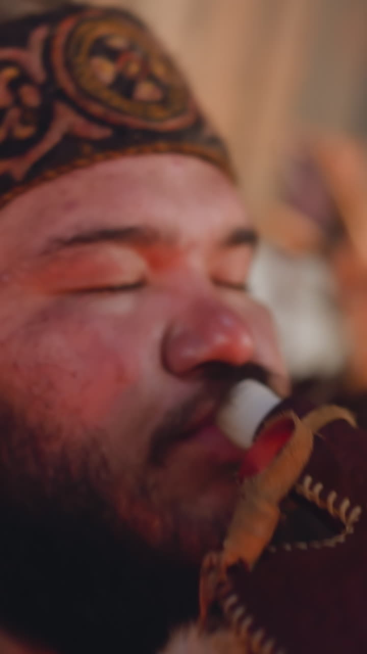 Tired plump man in national Altai clothes drinks from leather waterskin in cabin closeup. Traditional tribal pack for liquids carriage. Ethnic festival