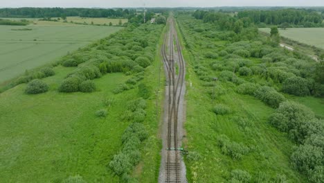 aerial establishing view of empty railroad train tracks, countryside scenery, fresh green forest on the side, overcast cloudy summer day, wide drone shot moving forward