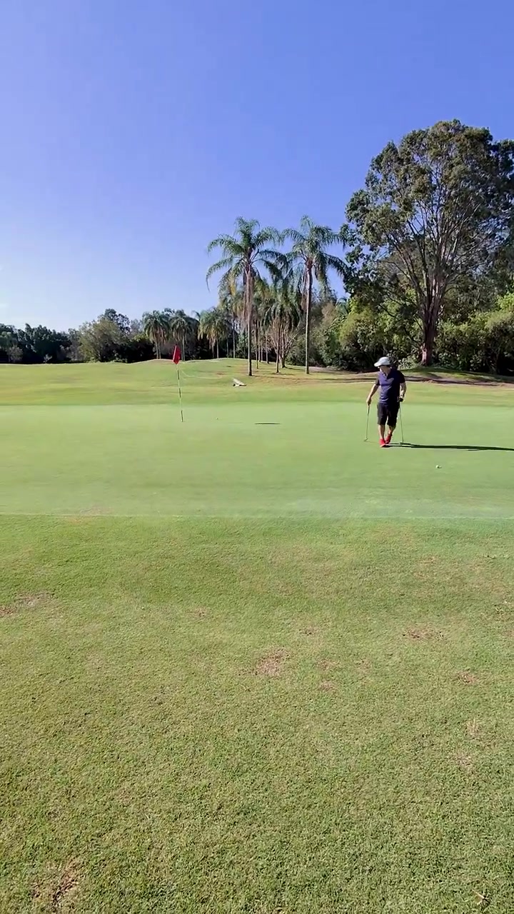 Colpo di golf chip in prima persona verso l'asta della bandiera su un campo luminoso e tropicale con telecamera a mano ferma.