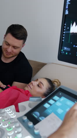female obstetrician checks the pregnant woman on ultrasonic equipment. future parents look attentively on the monitor. vertical video