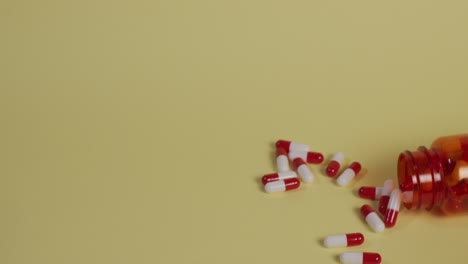 slow motion high-angle medium shot of a bottle of pills as it falls vertically, bounces, flips over and spills pills as it rolls off screen