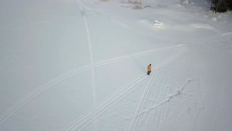 vista aérea de arriba hacia abajo de un anciano caminando en un sendero móvil de nieve, en un paisaje nevado de invierno, tiro de seguimiento inclinándose hacia abajo, en rovaniemi, finlandia