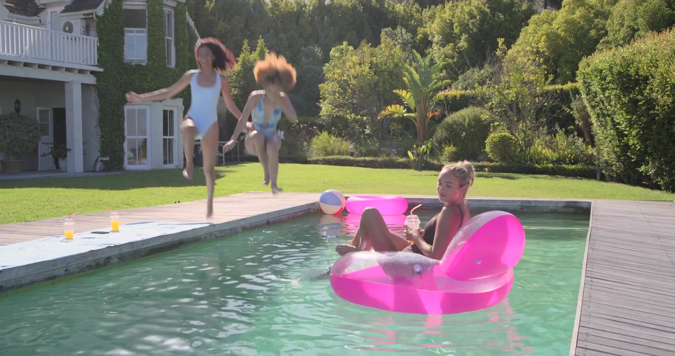 Women friends jumping into yard pool, splashing and pushing float, blonde steadying and sipping cup