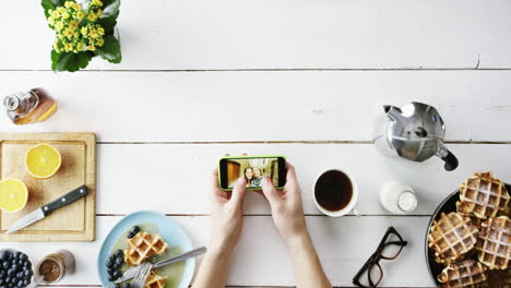 Top-view-man-browsing-vacation-photographs-using-smartphone-at-breakfast-Belgian-waffles-and-coffee-hands-from-above---Red-Epic-Dragon