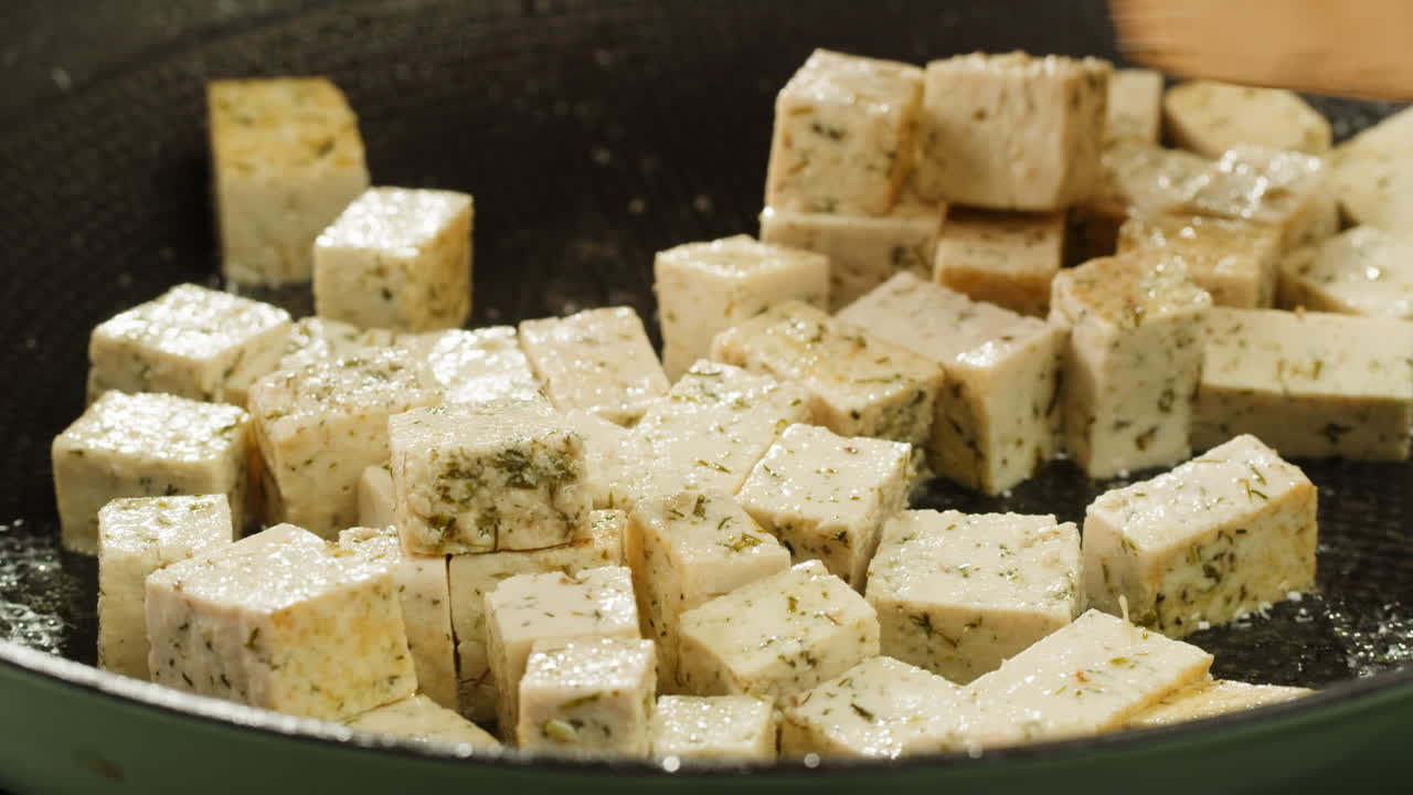 Fried tofu with sesame seeds and spices on cast iron pan, cooking japanese salad. Healthy ingredient for cooking vegan vegetarian diet food. Roasted tofu over black background.